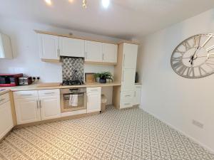 a kitchen with white cabinets and a clock on the wall at Stay @ Enville Close, Birmingham Airport & NEC in Marston Green