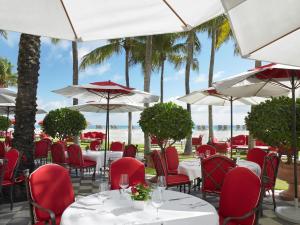 a restaurant with white tables and red chairs and palm trees at Acqualina Resort and Residences in Miami Beach