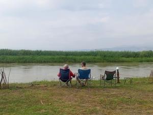 due persone sedute sulle sedie accanto a un corpo d'acqua di Semliki Fishing River Camp 