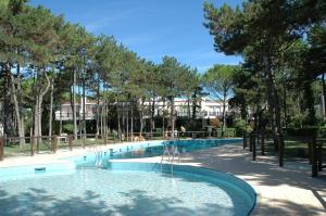 a swimming pool with trees and a building in the background at Villaggio Estate in Lignano Sabbiadoro