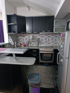 La cuisine est équipée de placards noirs et d'un réfrigérateur en acier inoxydable. dans l'établissement SKY APARTMENTS, à Kumanovo