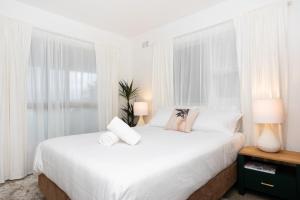 a white bedroom with a large white bed with windows at Beach View Mollymook in Mollymook