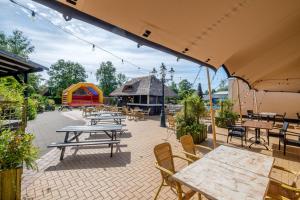 een patio met tafels en stoelen en een speeltuin bij Het Familie Boshuisje - vakantiewoning op prachtig park met veel faciliteiten inc ligbad in Gramsbergen