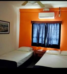 2 Betten in einem Zimmer mit orangefarbener Wand in der Unterkunft Hotel Mango Cafe in Tela