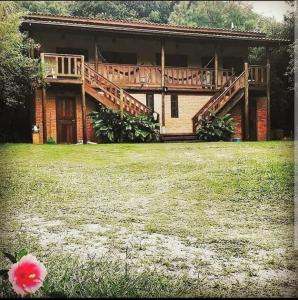 a house with a deck and a yard with a flower at Quinta do Urutau in Praia do Rosa