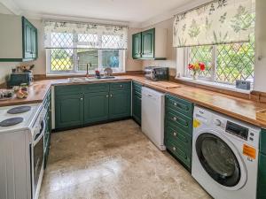 a kitchen with green cabinets and a washer and dryer at Pixies Wood Cottage in Ludham