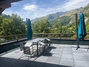a patio with chairs and umbrellas on a balcony with mountains at Châlets AOKI in Valloire