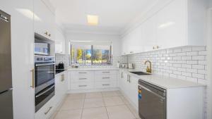 a white kitchen with white cabinets and a window at Hibbard Waterfront Escape in Port Macquarie