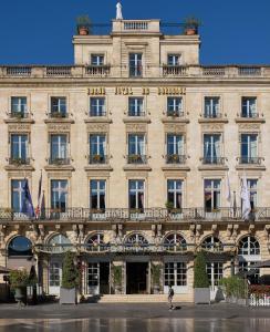 een groot gebouw waar een vrouw voor loopt bij InterContinental Bordeaux Le Grand Hotel, an IHG Hotel in Bordeaux