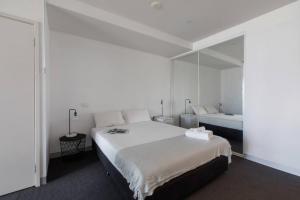 a white bedroom with a large bed and a mirror at Flinders Street Simplicity Overlooking the Yarra in Melbourne