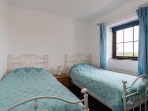 two beds in a bedroom with blue curtains and a window at The Schooner in Goleen