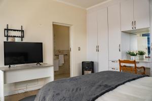 a white bedroom with a bed and a flat screen tv at 3 on Tessa Guesthouse in Johannesburg