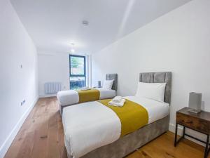 two beds in a room with white walls and wood floors at Heathrow Airport Apartments by Elegance Living in Hounslow