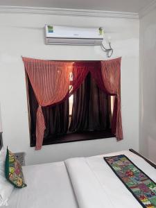Ce lit se trouve dans un dortoir doté d'une fenêtre avec des rideaux rouges. dans l'établissement Jaisalmer Hotel Meotrips, à Jaisalmer