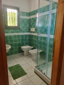 uma casa de banho com azulejos verdes, um WC e uma cabina de duche em vidro. em Casa vista mare golfo di Budoni em Budoni