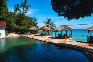 a swimming pool with chairs and umbrellas next to the ocean at Japamala Resort by Samadhi - Adults Only in Tioman Island