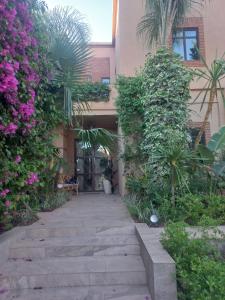 einen Gang, der zu einem Gebäude mit Pflanzen und Blumen führt in der Unterkunft Villa rouge in Marrakesch