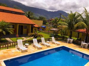 uma piscina com espreguiçadeiras e uma casa em Chalés Flamboyant em Caraguatatuba