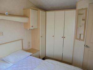 a small bedroom with a bed and white cabinets at Golden Sands: Richmond GS:- 6 berth, Blow heated, Access to the beach in Ingoldmells