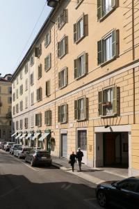 dos personas caminando por una acera en frente de un edificio en Brera Apartments in San Fermo, en Milán
