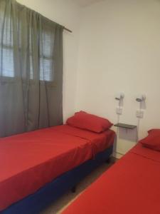 2 Betten in einem Zimmer mit roter Bettwäsche und einem Fenster in der Unterkunft Pachá Hostel Backpack in Salta
