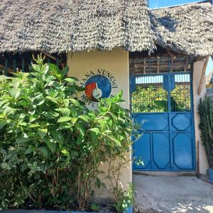 a house with a blue door and a thatched roof at MaNa Nungwi in Nungwi