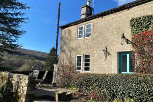 una casa de piedra con una puerta azul y una valla en Bridgefoot Cottage, en Froggatt