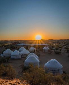 Kyzylkum Nights Camp & Family Yurt في Nurota: مجموعة من القباب في الصحراء عند غروب الشمس