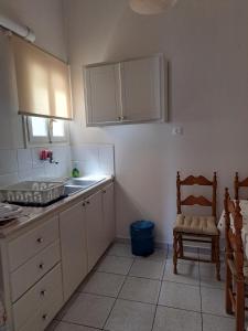 uma cozinha com armários brancos, uma cadeira e um lavatório. em Penny's Beach Cottage em Galaxidi