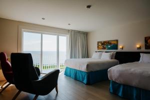 a hotel room with two beds and a chair and a window at Riotel Perce in Perce
