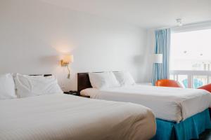 two beds in a hotel room with a window at Riotel Perce in Perce
