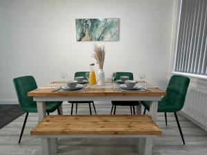 米德爾斯伯勒的住宿－Entire Modern Home Middlesbrough，餐桌、绿椅和带玻璃杯的木桌