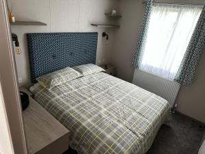 a bedroom with a bed with a plaid blanket and a window at Fairway 6 Lilliardsedge Caravan Hire in Jedburgh