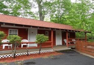 une cabane en rondins avec une véranda et des chaises blanches dans l'établissement Seven Dwarfs Motel & Cabins, à Lake George