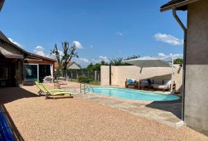 a swimming pool with chairs and an umbrella at Le Mas aux Papillons in Vendat