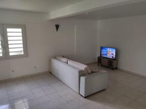 Una sala de estar blanca con un sofá y un televisor. en Appartement F3 ventilé, en Le Robert