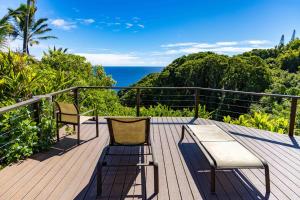 a wooden deck with two chairs and the ocean at Plumeria Room on a Lush Farm on Maui's North Shore in Huelo