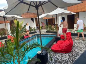 a group of people standing around a swimming pool with an umbrella at Cape Rose in Gili Trawangan
