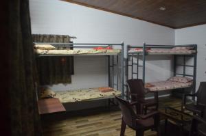 a room with three bunk beds with chairs and tables at The Meadows INN in Kottayam
