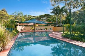 a swimming pool with an umbrella in a yard at Byron Links Apartments in Byron Bay