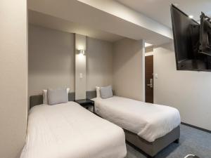 a hotel room with two beds and a flat screen tv at Tabist Unihotel Midosuji Hommachi in Osaka