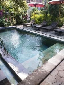uma piscina com duas mesas de piquenique e guarda-sóis em ComeBack GuestHouse em Canggu