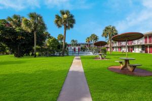 a path through a park with two picnic tables and palm trees at HomeTowne Studios by Red Roof Vero Beach - I-95 in Vero Beach