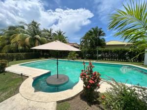 uma piscina com um guarda-sol e uma mesa com flores em Las Veraneras Villa - Pet Friendly em Acajutla