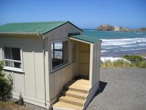 a small building with a door and stairs next to the beach at Castlepoint Holiday Park & Motels in Castlepoint
