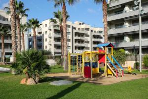 une aire de jeux dans un parc avec des palmiers et un bâtiment dans l'établissement AT157 Nova Torredembarra II, à Torredembarra
