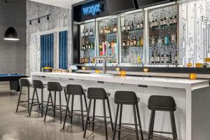 a bar with stools in a room with alcohol bottles at Aloft Chicago Schaumburg in Rolling Meadows