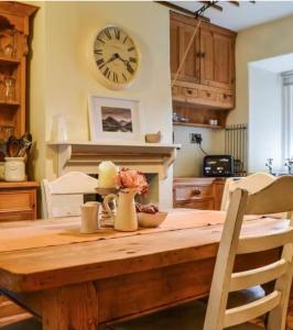 a kitchen with a wooden table with a clock on the wall at Roses Cottage - near Scafell Comfy Modern Idyllic in Santon Bridge