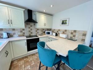 a kitchen with white cabinets and a table with blue chairs at Seagull Leigh Cottages in Seaton