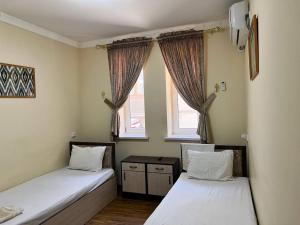 two beds in a room with two windows at Ikat Terrace in Bukhara
